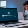Frustrated person looking at a slow laptop with a stuck Windows update progress bar on the screen.