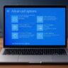 Laptop open on a wooden table displaying the blue Windows Advanced Options recovery menu screen with troubleshooting tools.